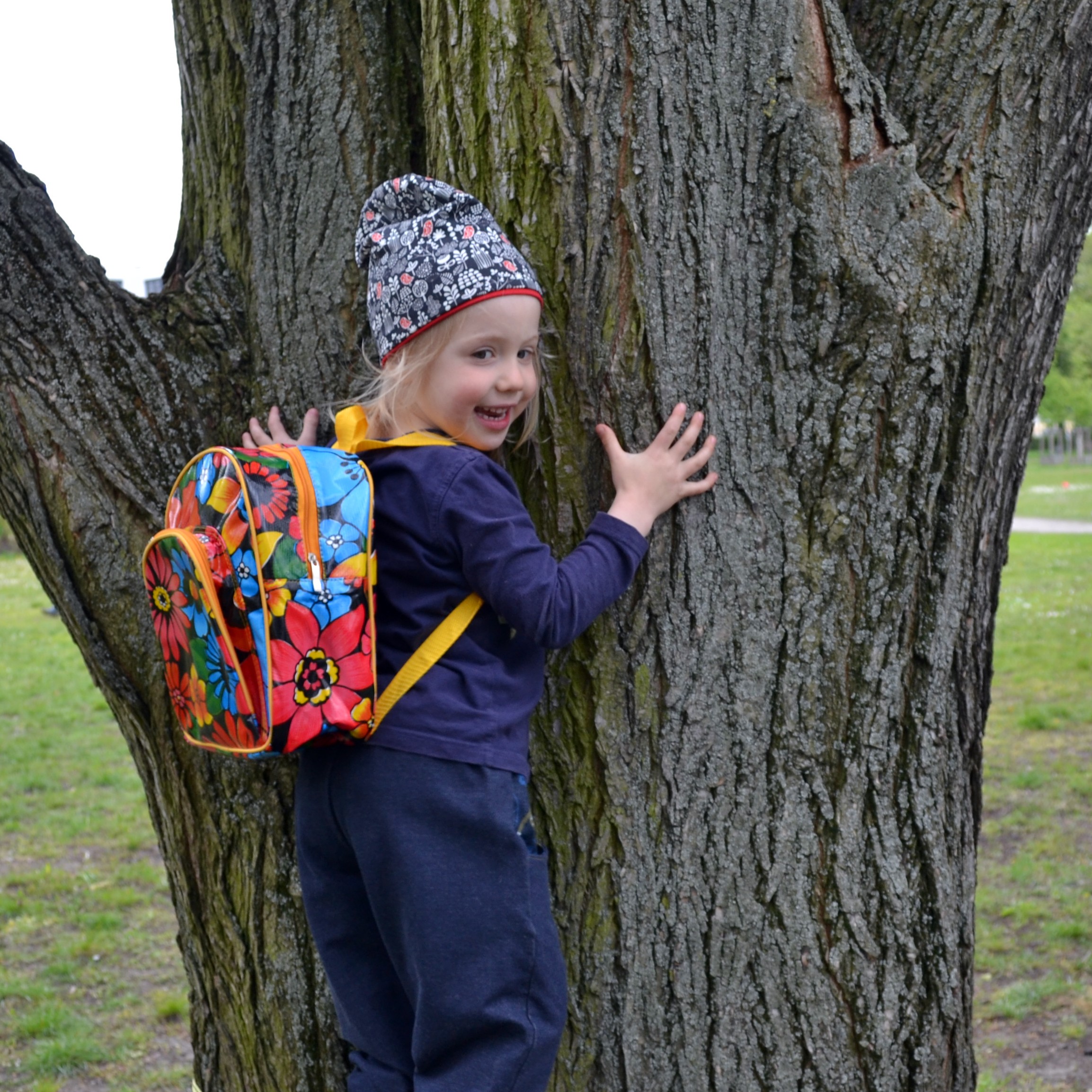 Kind trägt den bunten Kinderrucksack Alegria an einem Baum