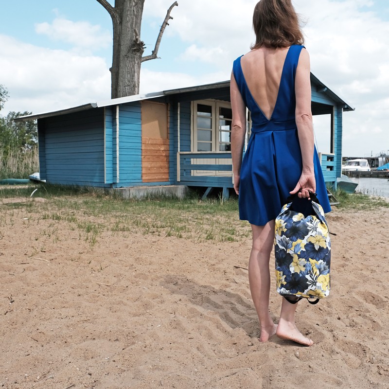 Frau im blauen Kleid hält den Drybag Azucena am Sandstrand