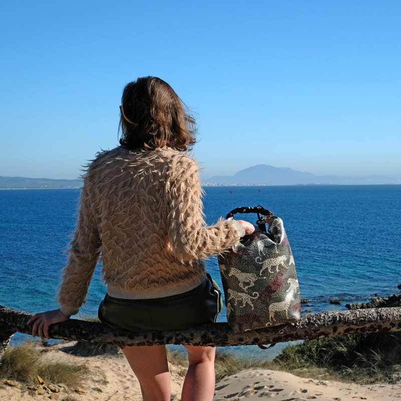 Frau sitzt mit dem Drybag Animals auf einem Baumstamm über dem Meer