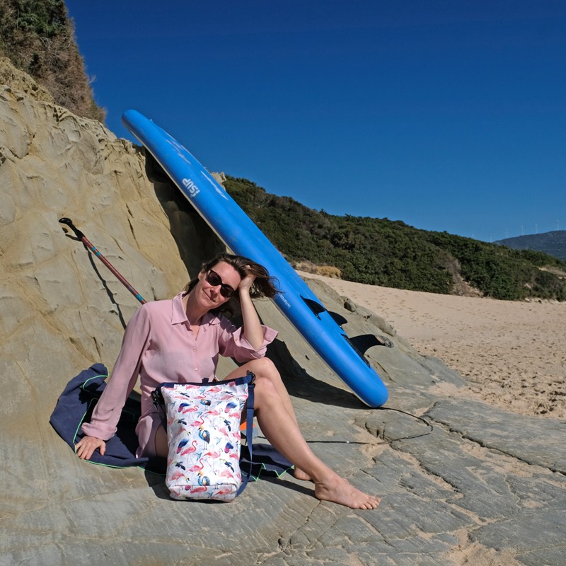 Frau sitzt vor einem SUP-Board, neben ihr der Drybag Pajaros