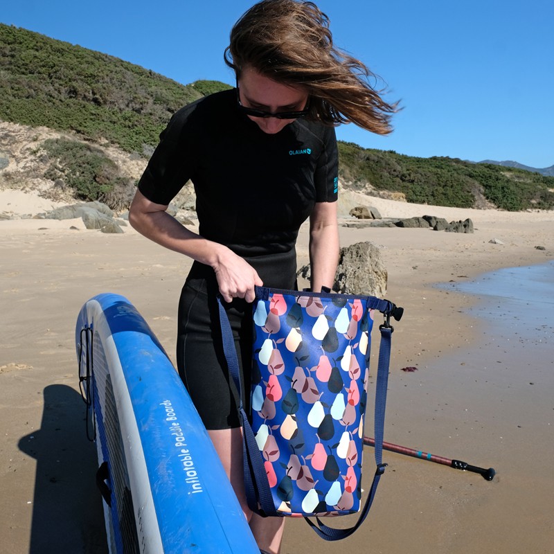 Frau hält den wasserdichten Rucksack Peras blau am Strand