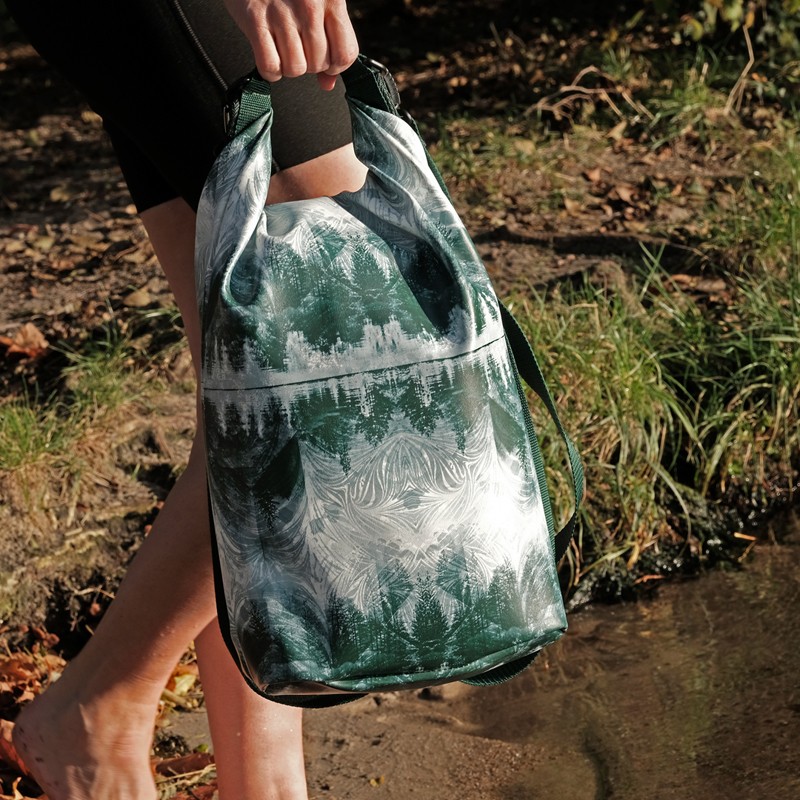 Drybag Pinos mit Tannen-Muster in der Hand am Wasser