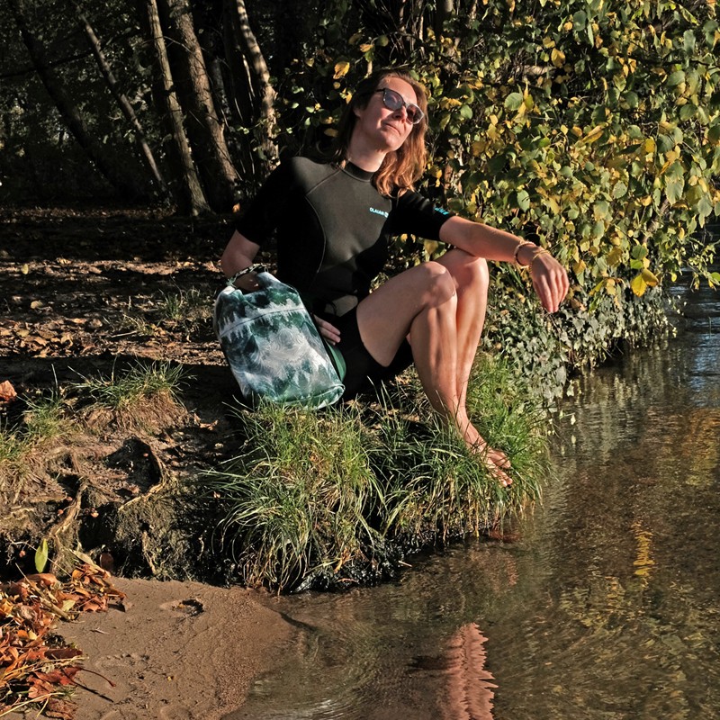 Frau sitzt mit dem wasserdichten Rucksack Pinos am Seeufer