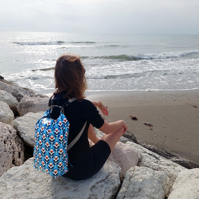 Frau sitzt mit dem wasserdichten Rucksack Scandinavia auf Felsen am Strand