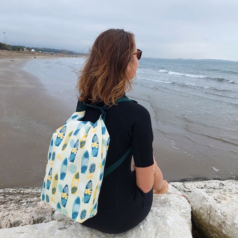 Frau sitzt mit dem wasserdichten Rucksack Surf auf einem Felsen am Meer