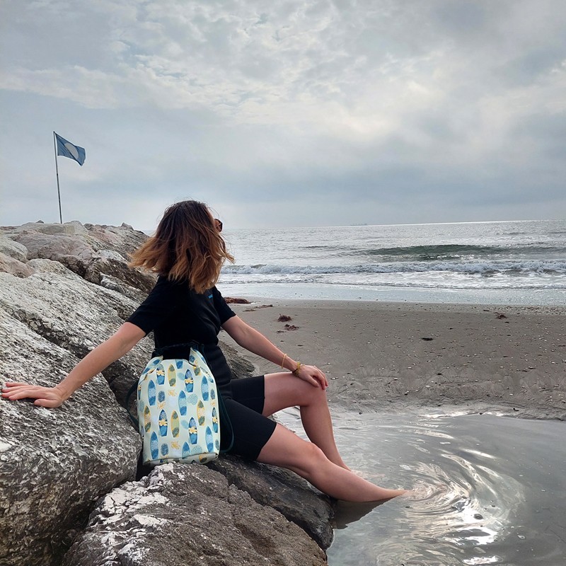 Frau mit Drybag Surf sitzt am Wasser auf den Felsen