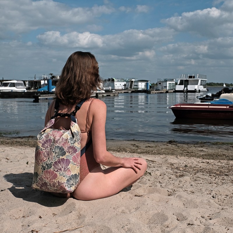 Frau sitzt am Strand mit dem Drybag Veranillo auf dem Rücken
