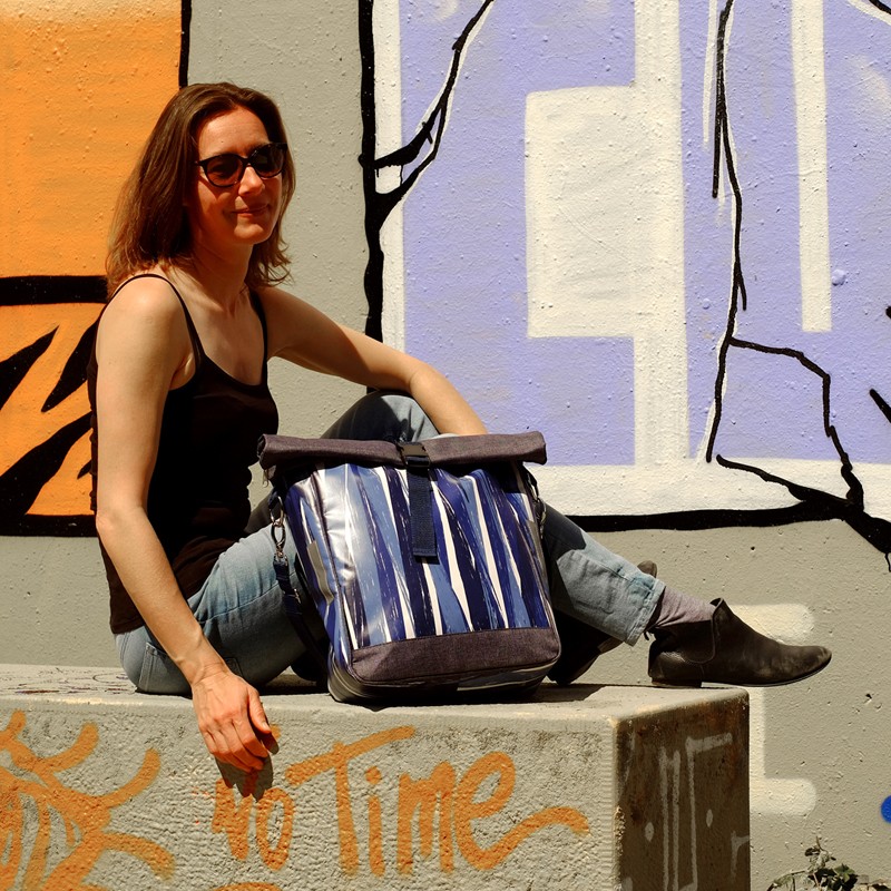 Frau sitzt vor einer bunten Wand mit der Tasche Indigo
