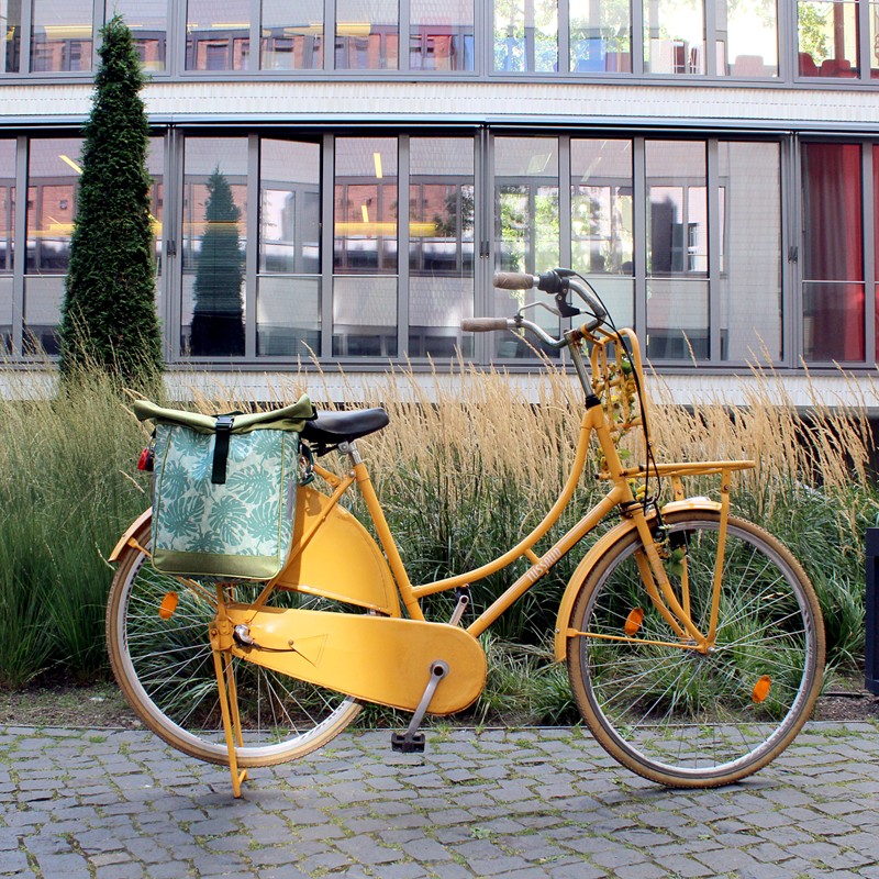 Gelbes Fahrrad mit Seitentasche Monstera in der Stadt