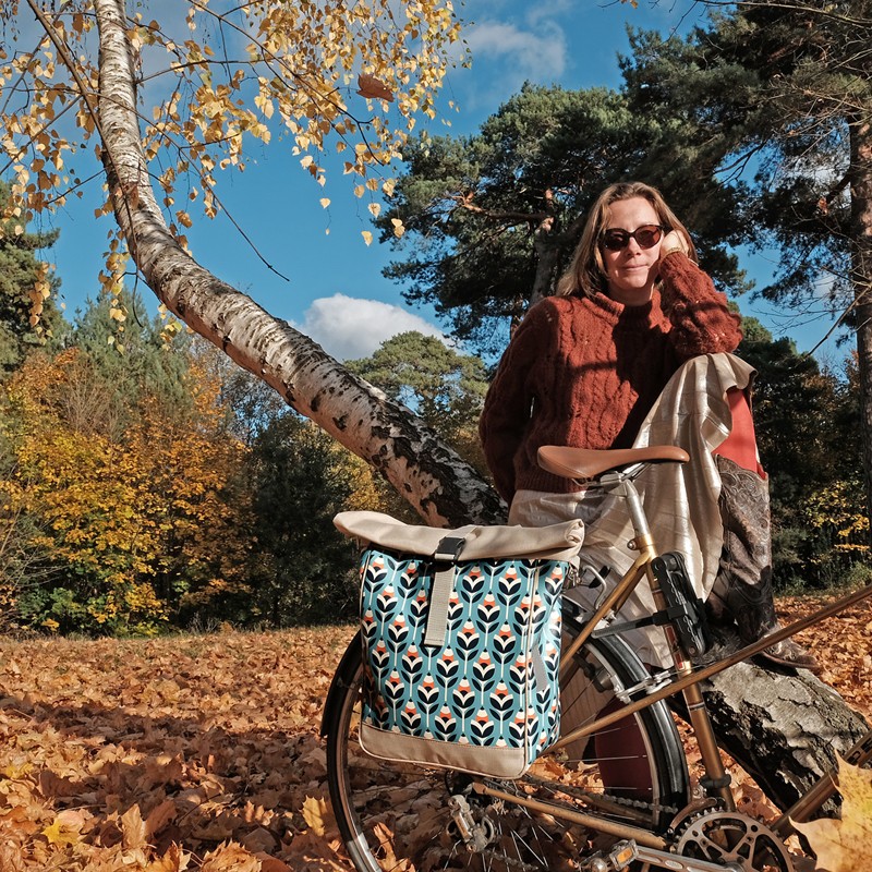 Frau sitzt im Herbstwald, neben ihr die Fahrradtasche Scandinavia