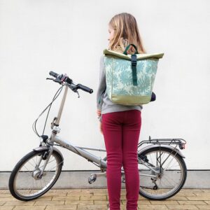 Mädchen trägt den kleinen Rucksack Monstera von Ikuri neben einem Klapprad