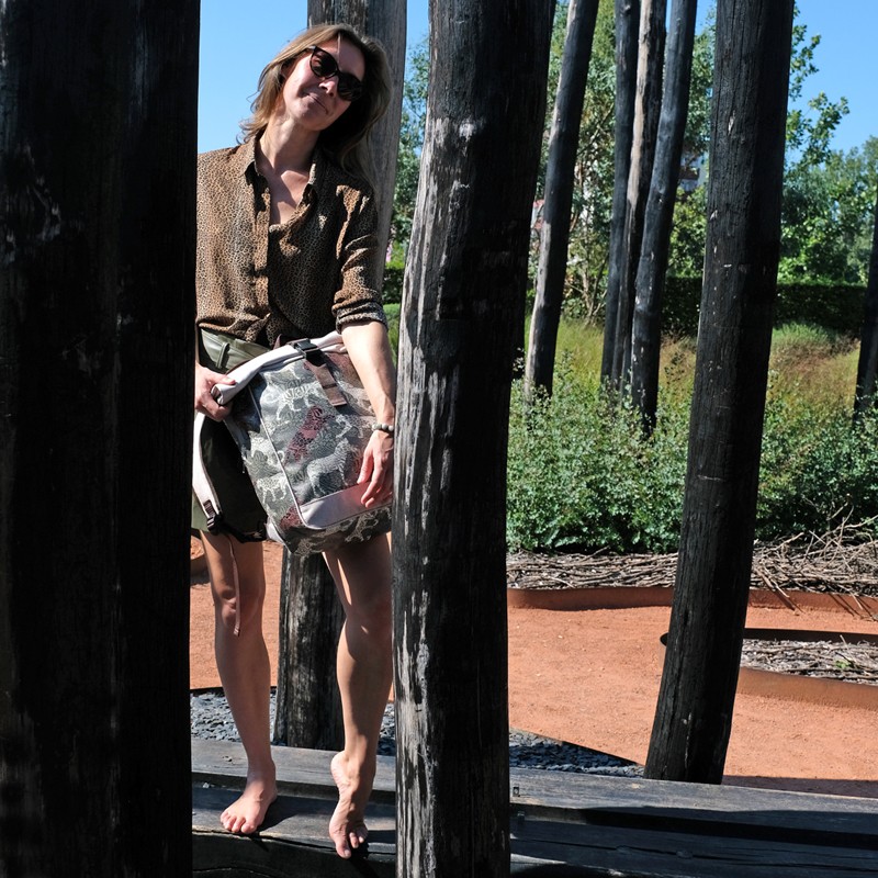 Frau hält den Fahrradrucksack Animals mit Leoparden-Print zwischen Holzpfählen