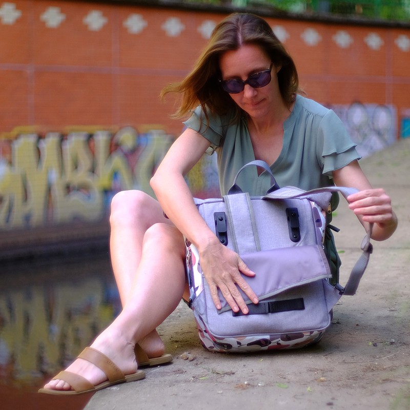 Frau sitzt am Kanal und öffnet den Fahrradrucksack Damen Peras