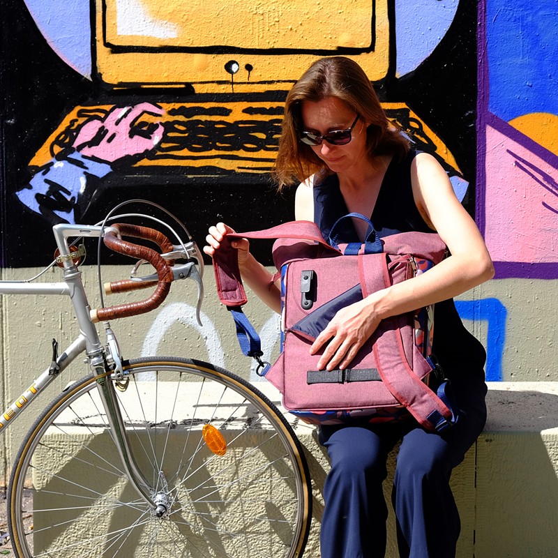 Frau sitzt neben dem Fahrrad und öffnet die Fahrradtasche Peras blau