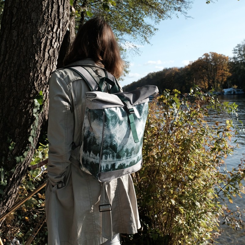 Frau im Trenchcoat trägt den Fahrradrucksack Pinos als Rucksack am Fluss