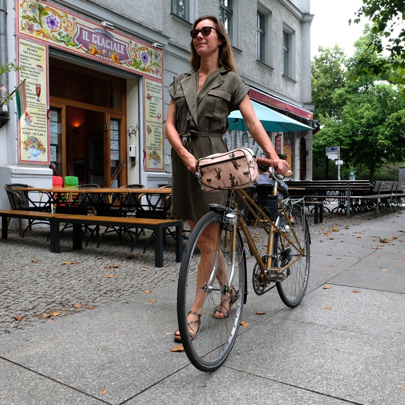 Frau schiebt ihr Fahrrad mit Lenkertasche Cactus durch die Stadt