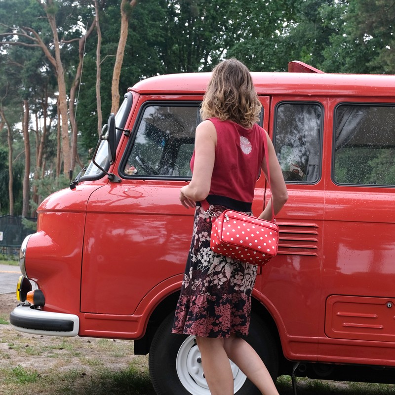 Frau trägt die Lenkerhandtasche Lunares rot vor einem roten Auto