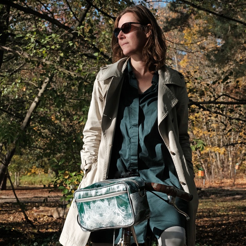 Frau schiebt ihr Fahrrad mit Lenkertasche Pinos durchs Herbstlaub